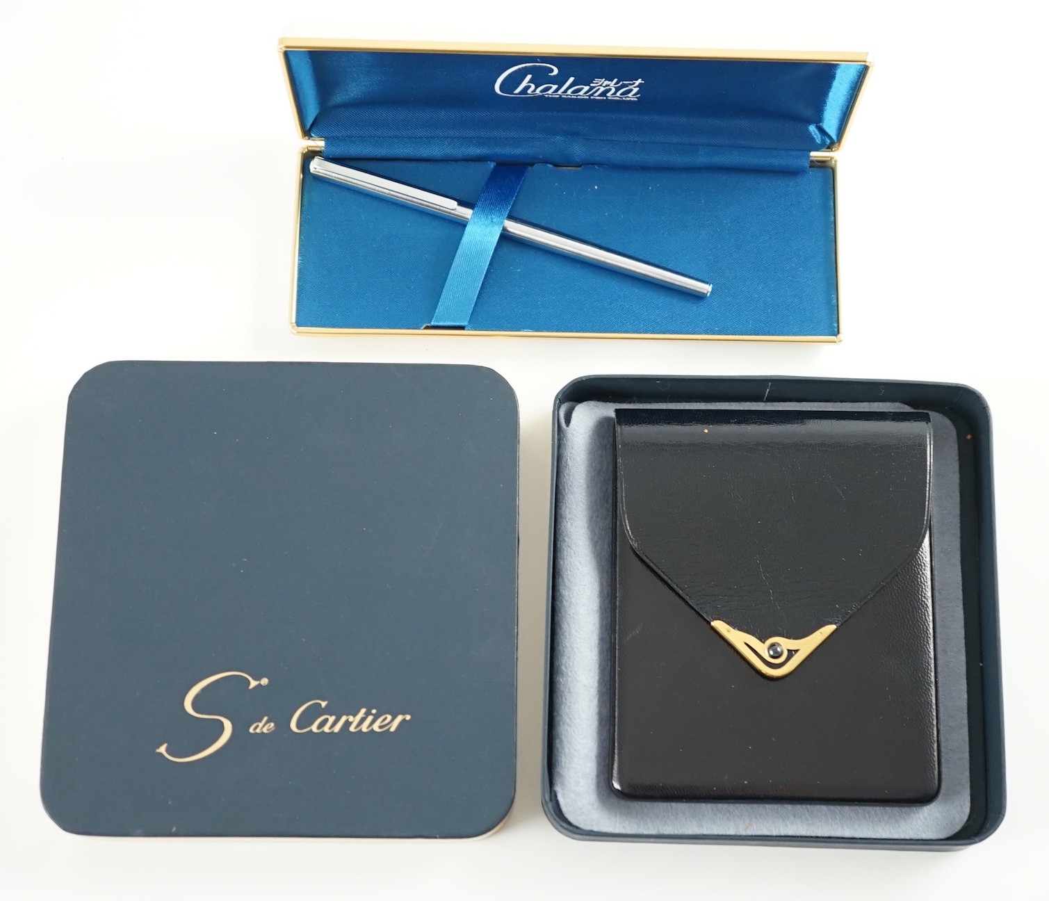 An S de Cartier navy blue leather cigarette case with blue cabochon set clasp, 11 cm., boxed and a Chalana note pen, cased.